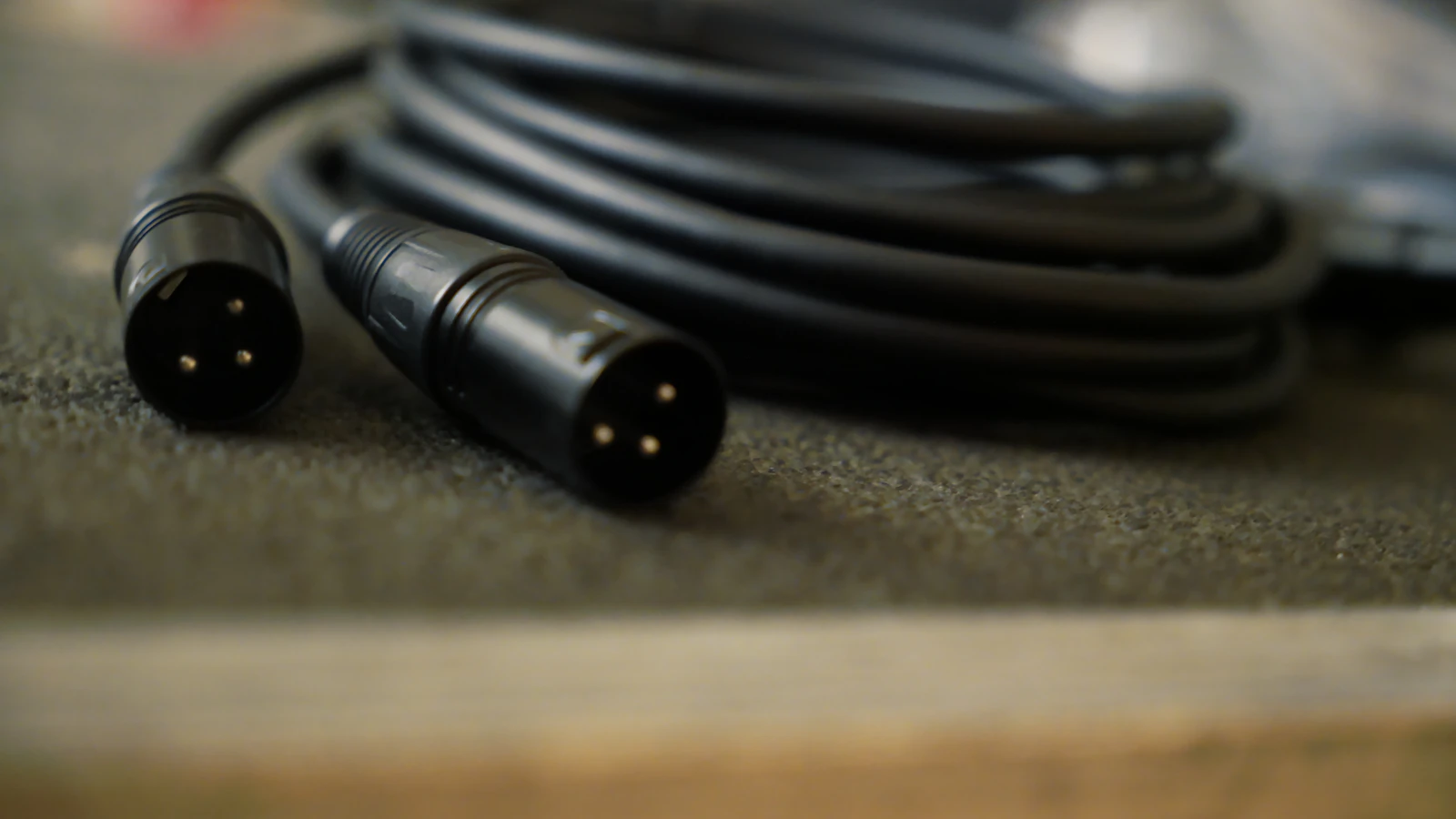 שני תקעי XLR שחורים עם שלושה פינים, מונחים על משטח לצד כבל שחור מגולגל