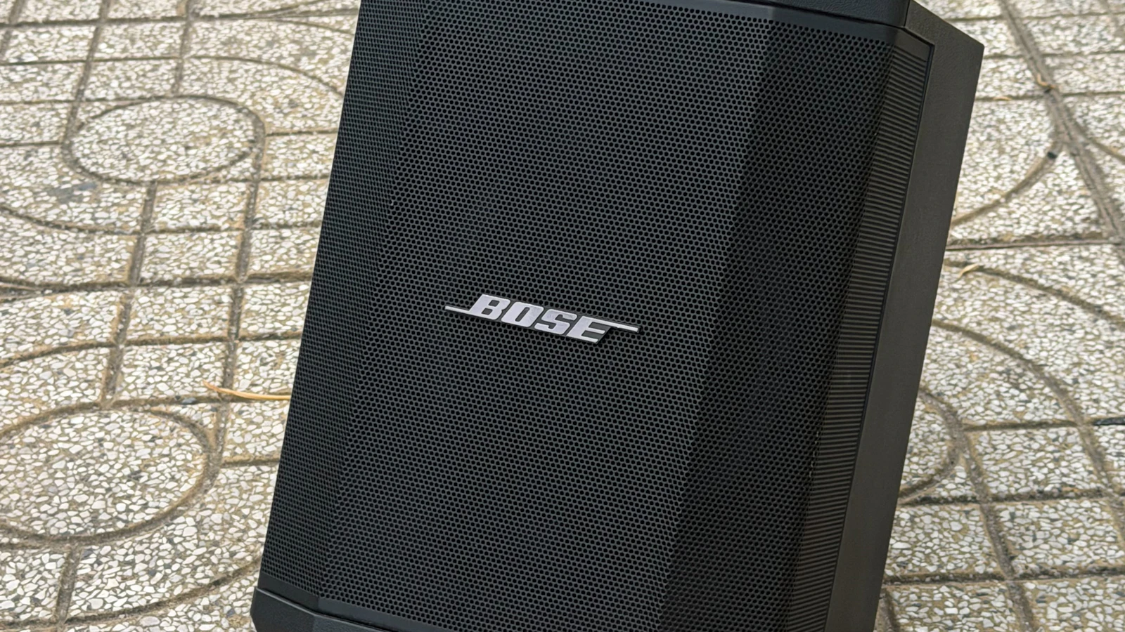 רמקול נייד שחור של Bose בצורת קופסה עומד על מרצפות מעוטרות בחוץ