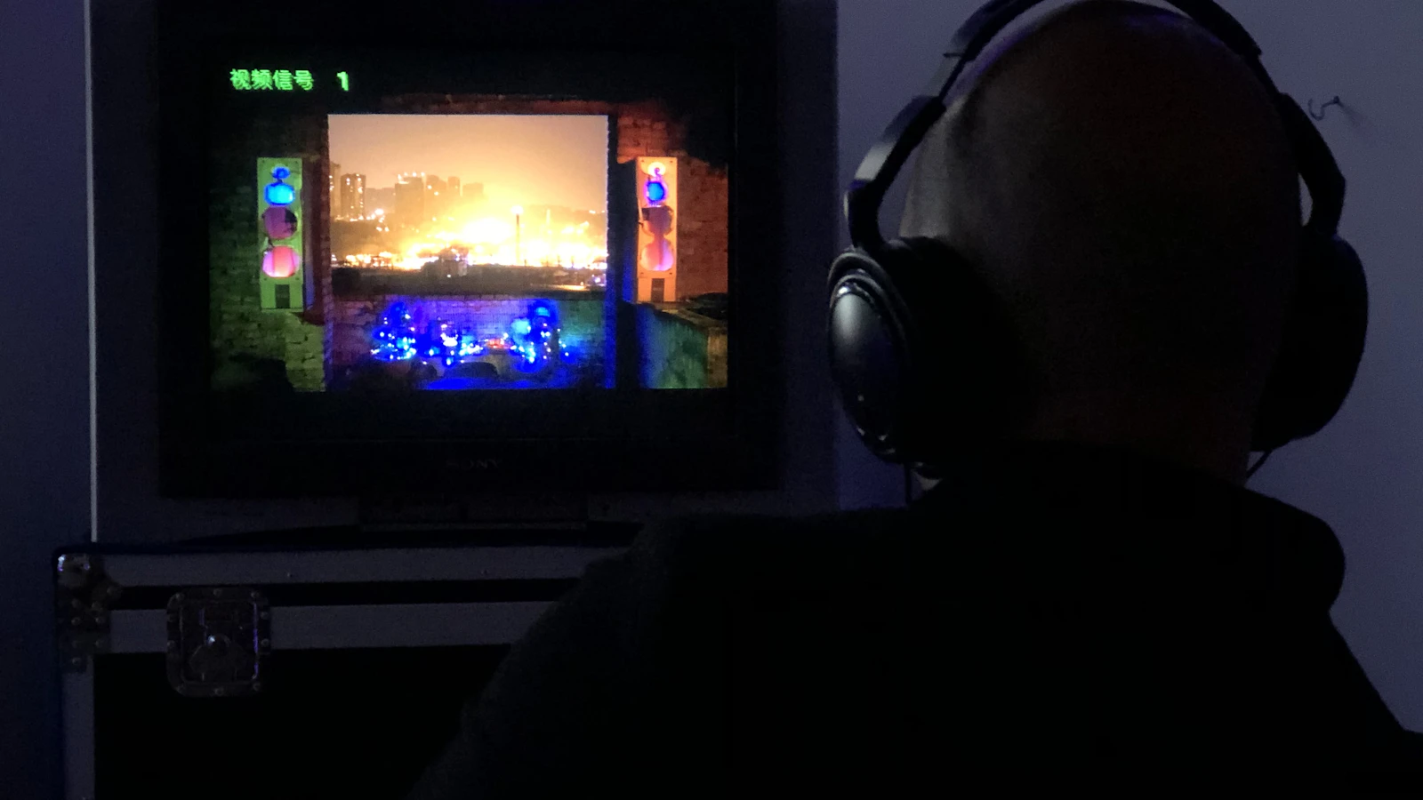אדם עם אוזניות קשת גדולות יושב בחדר חשוך מול טלוויזיה ישנה